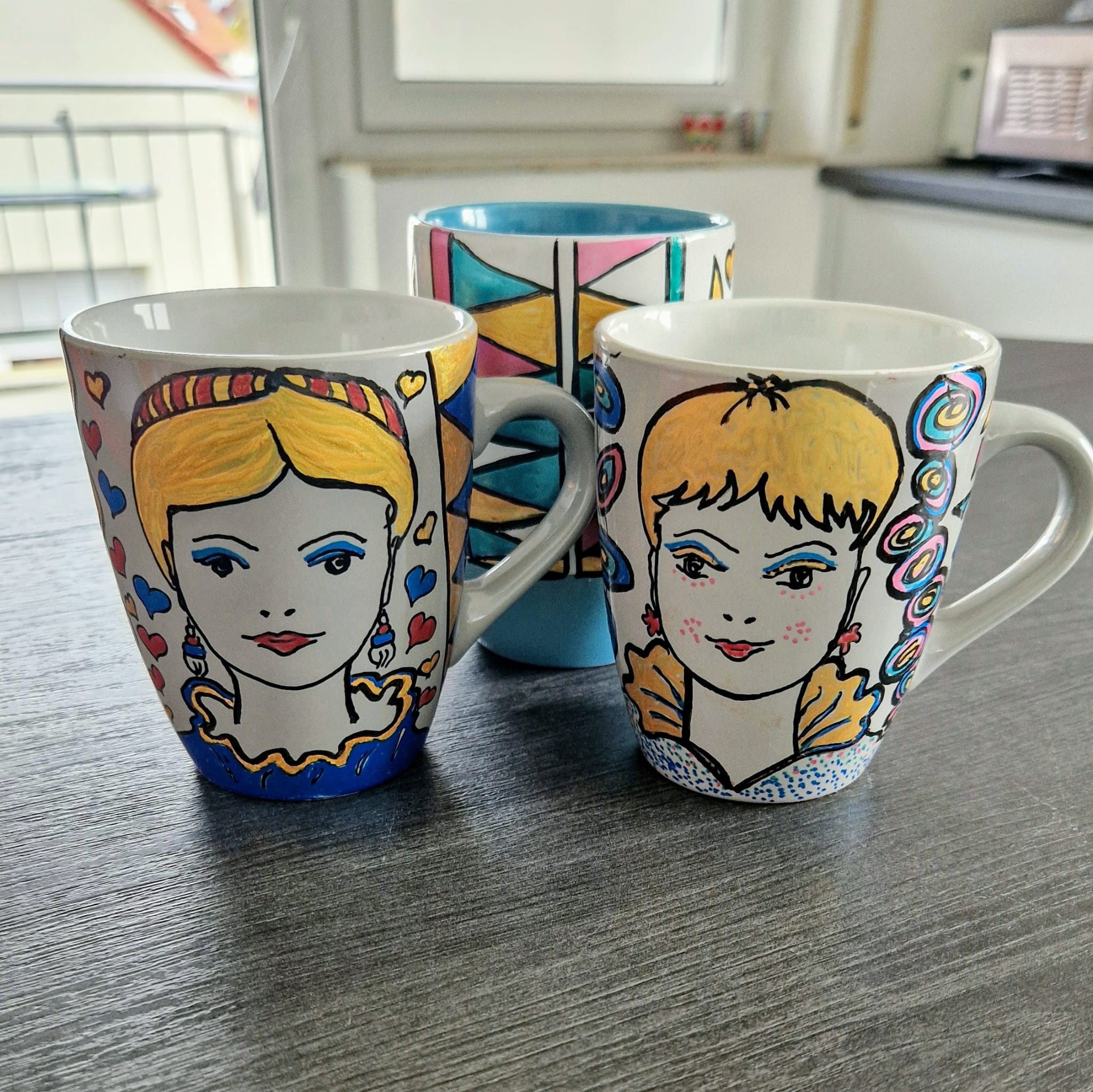 Drei Tassen bemalt mit Frauengesichtern und Mustern